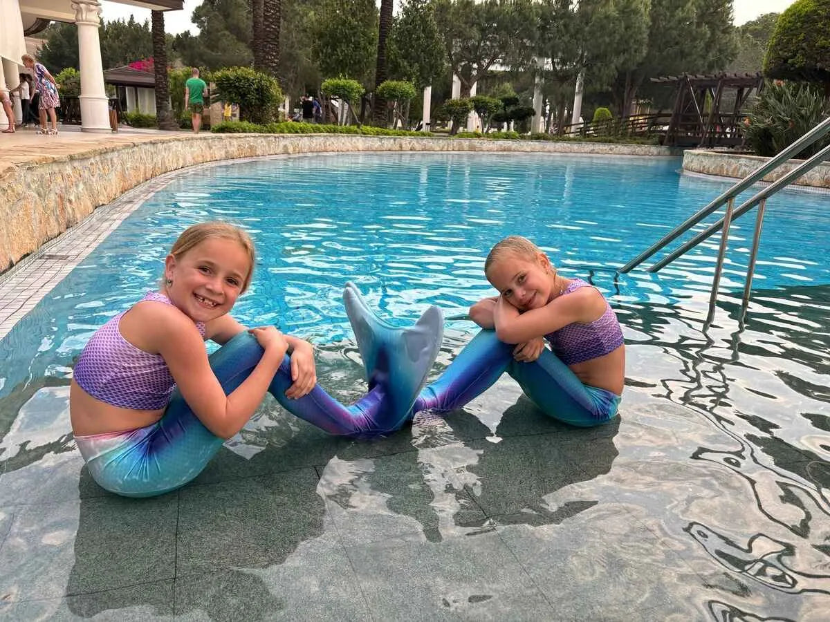Twee kinderen in kleurrijke zeemeerminstaarten zittend bij een zwembad